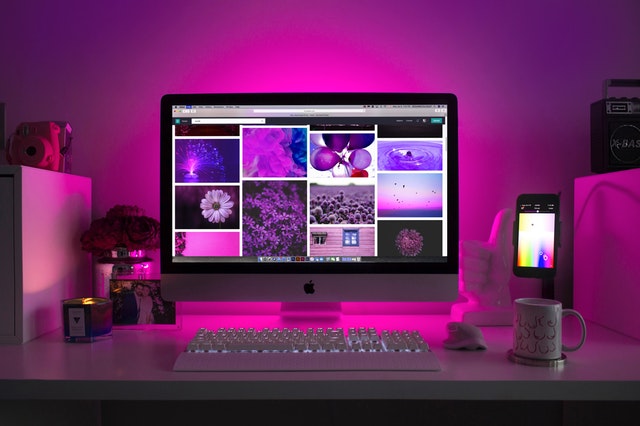 Počítač na pracovnom stole s fotografiami na obrazovke a ružové osvetlenie
