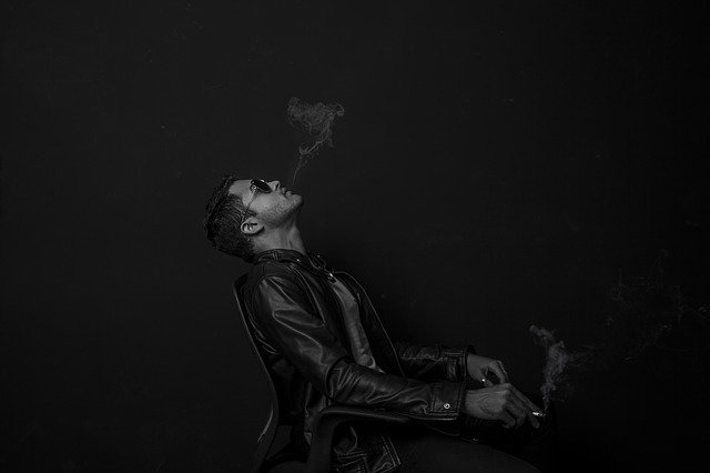 Muž koženej bunde fajčí a vyfukuje dym 